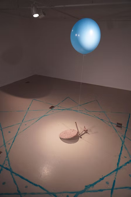 A floating blue balloon attached to a clay covered satellite dish and blue line drawing on the floor
